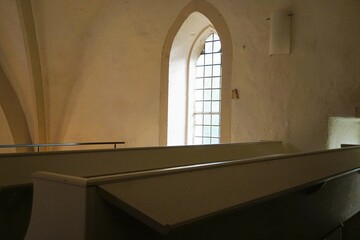 Innenausstattung von Kirche mit weißen Holzsitzbänken,  weißer Wand und großen langen Fenster...