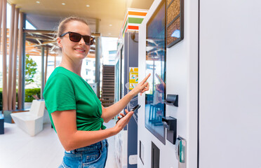 Young woman paying for coffee at vending machine using contactless method of payment  - obrazy, fototapety, plakaty