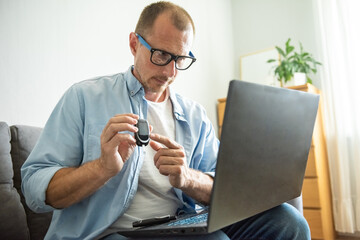 Diabetic patient man using glucose meter for measuring and monitoring blood level showing your measurement level to doctor via laptop. Online medical consultations, telemedicine concept - obrazy, fototapety, plakaty