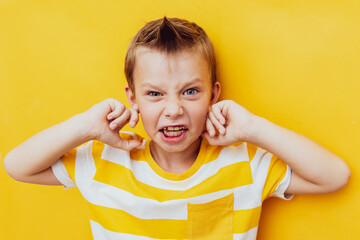 Angry crazy scared teen boy covering ears screaming feeling annoyed, stubborn stressed outraged young boy. Isolated on yellow studio background - obrazy, fototapety, plakaty