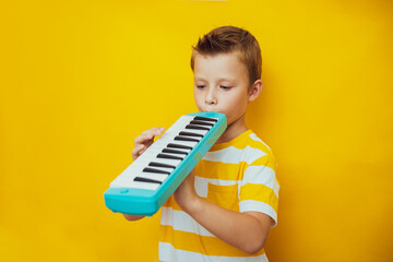 Cute child boy play the keyboard harmonica, yellow background