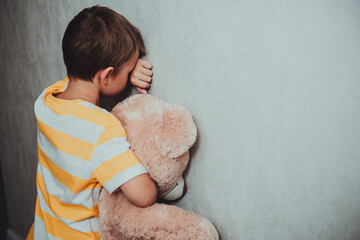 A little boy cries in the gray corner, hiding his face and hugs the teddy bear. Krnsception:...