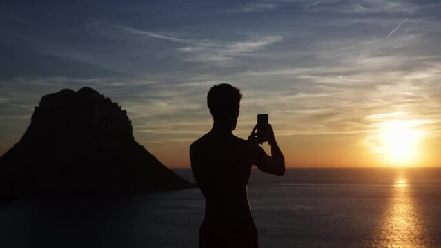 Man on a viewpoint holding the mobile phone with both hands to take a photo vertically.