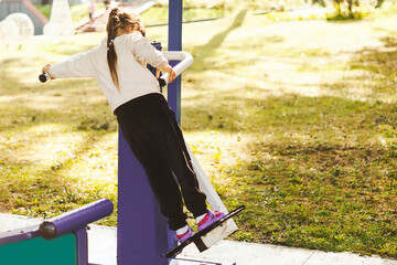 Cute little girl training on sports equipment. Happy little girl training on a simulator on an outdoor sports ground. A five-year-old girl is doing fitness on a simulator. Happy childhood concept