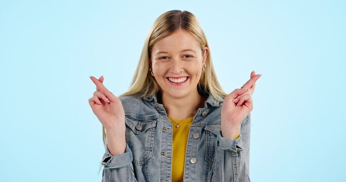 Fingers crossed, happy and face of woman hope for success, waiting for luck and results in studio on blue background. Portrait, model and praying for bonus, winning lotto prize and wish of emoji sign