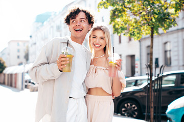 Young smiling beautiful woman and her handsome boyfriend in casual summer clothes. Happy cheerful family. Female having fun. Couple posing in street. Holding and drinking cocktail drink in plastic cup