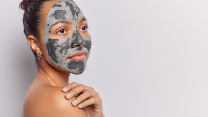 Beauty procedures concept. Sideways shot of serious Latin woman applies clay mask for skin...