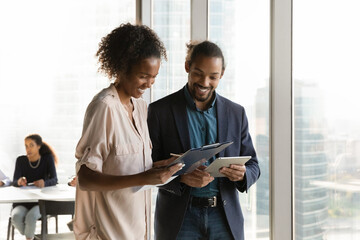 Smiling African American businesswoman and businessman discussing project, standing in modern...