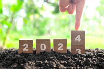 Human hand change year 2023 to 2024 in wooden blocks with growing plant at sunrise. Welcome new...