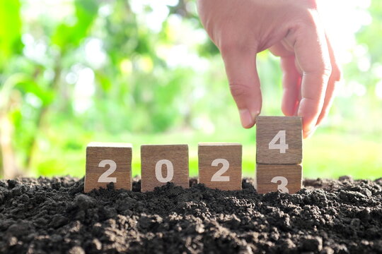 Human hand change year 2023 to 2024 in wooden blocks with growing plant at sunrise. Welcome new year 2024 and goodbye 2023 concept.