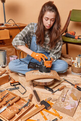 Photo of young concentrated skilled European lady sitting on floor of handicraft workshop with...