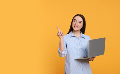 Smiling young woman with laptop on yellow background, space for text