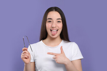 Happy woman showing tongue cleaner on violet background - obrazy, fototapety, plakaty