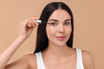 Beautiful woman applying serum onto her eyelashes on beige background. Cosmetic product