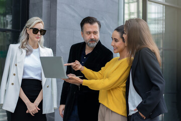 Group of business people talking and discussing strategy, business brochure, working together using laptops outside outdoor office