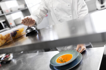 food cooking, profession and people concept - close up of male chef with plate of pumpkin cream soup ringing bell at restaurant kitchen table