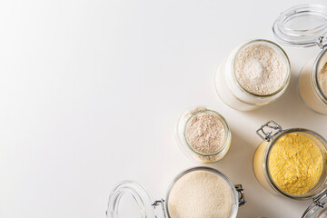food storage, culinary and eating concept - close up of jars with different kind of flour on white background, top view