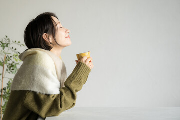 コーヒーや紅茶を飲むニットを着た女性　目を閉じる