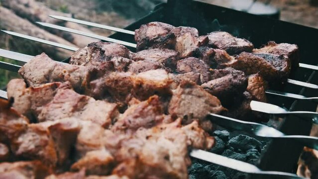 Shish kebabs on skewers are cooked on the grill in nature outdoors. Roasted juicy pork meat is fried on metal skewers on the BBQ, close-up. Barbecue on charcoal with smoke at a summer picnic. 4K