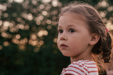 Close-up. Portrait of cute serious little girl looking to side at sunset in summer. Childhood.