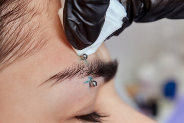 Professional placing the jewel of piercing on the temple on the head with ball. Tragus type.