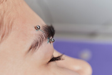 Professional placing the jewel of piercing on the temple on the head with ball. Tragus type.