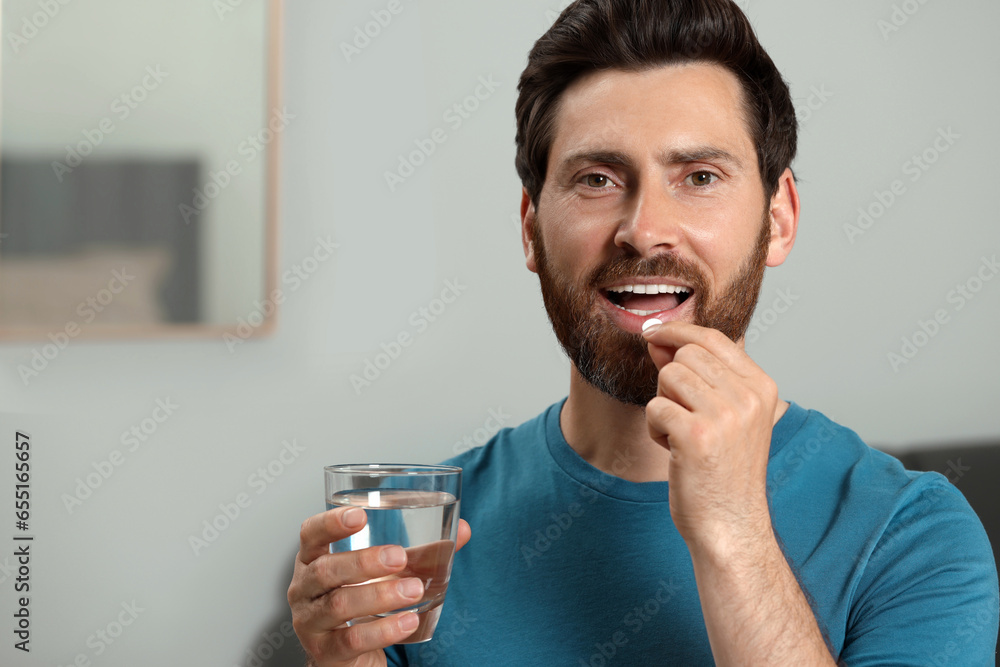 Canvas Prints Handsome man with glass of water taking pill indoors, space for text