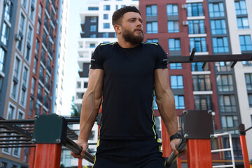 Man training on parallel bars at outdoor gym, low angle view