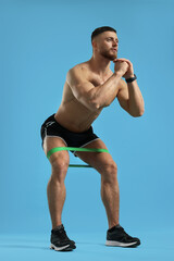 Muscular man exercising with elastic resistance band on light blue background