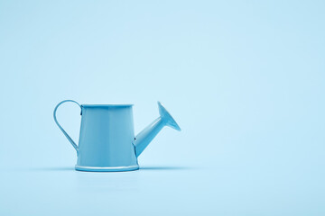 Bright blue garden watering can on the surface of the bright solid fond plain bright blue background