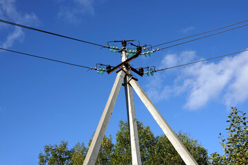 Top of pylon of power supply line with wires and insulators in rural place under blue sky with white clouds