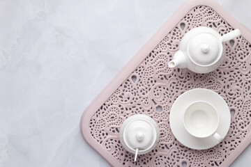 Fototapeta na wymiar Morning tea party. White ceramic teapot, cup and sugar bowl on a pink openwork tray. Gray marble background. Table setting, flat lay, top view. Serving space, clean ceramic dishes. Empty tableware.