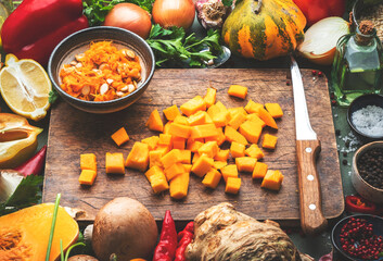 Food background. Diced raw peeled pumpkin and vegetable knife on rustic wooden cutting board....