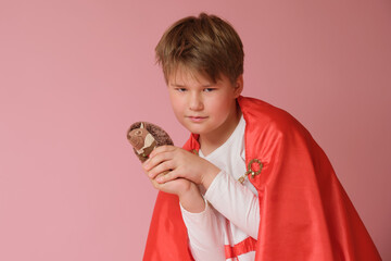 Little boy dressed like superhero holding a toy on pink background