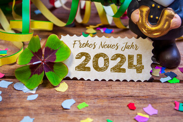 Wooden hang tag and slate with four leaf clover and sparklers with the german words for happy new year - frohes neues jahr 2024 on wooden weathered background - obrazy, fototapety, plakaty