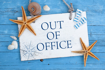 Wodden sign with message out of office with mediterranean decorative items on blue weathered background