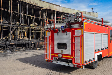 Fire service vehicle. Burnt building. Fire service truck. Rear view fire extinguishing machine. Car for firefighters near burnt building. Ruins house damaged by flame. Firefighters transport
