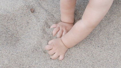 Baby enjoying putting his hands in sand at a beach.