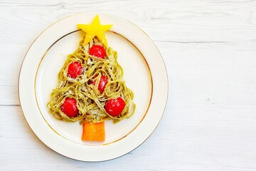 Christmas tree pasta made it from spinach tagliatelle pasta,tomatoes,carrot,parmesan cheeses and yellow bell peppers on plate with white wood background.Creative art food idea for Christmas's dinner

