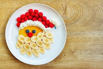 Santa claus pancake made it from pancake,bananas,blueberries,raspberries and whipped cream on plate...