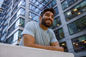 Handsome man in sporty clothes standing against backdrop of skyscrapers with smile
