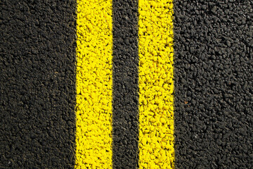 Close-up yellow dividing lines on the road with copy space. Yellow double solid line. Road markings on asphalt. Gray asphalt background with two yellow road lines. Black asphalt - obrazy, fototapety, plakaty
