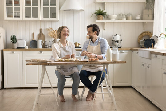 Attractive young couple wear aprons spend time together in the kitchen, knead dough for home-made pastries, buns or dumplings, prepare biscuits for family holiday. Family recipe and traditions, date