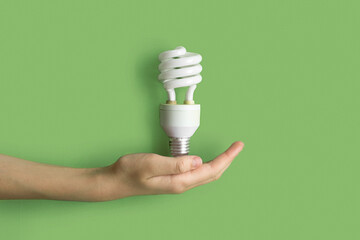 Compact fluorescent lamp Lamp in human hand. Helical integrated CFL Lightbulb on green pastel color background. Idea, creativity concept. Flat lay design. Banner, top view photo. Mockup. Lighting, eco