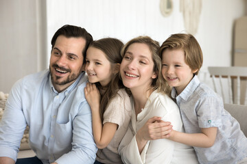 Fototapeta premium Friendly dreamy couple and children looking away rest on sofa at new apartment, parents enjoy spend time together with two little kids, have fun, show love and care. Family portrait of two generation
