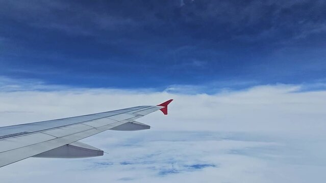 Aircraft wing flying above clouds with blue sky from airplane window view.