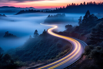 Car headlights and traffic lights on a winding road through pine trees, in a foggy valley at sunset, captured by long exposure photography