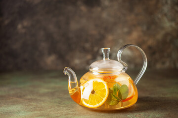 Glass teapot with hot citrus tea from oranges, lemons, apples and mint. Healthy drink on  dark...