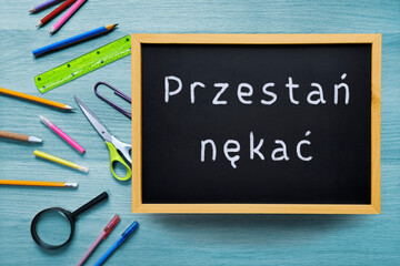 Stop bullying. IInscription in Polish Przestań nękać with chalk on black school board. Anti-bullying text on backdrop of school supplies. Concept of protecting children from bully in Poland.