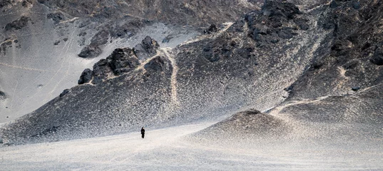 Rolgordijnen A woman standing in front of a huge black mountain. © imphilip